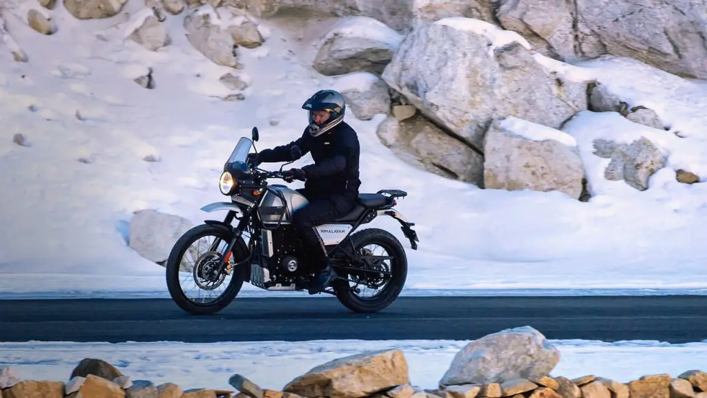 A man riding a Royal Enfield Himalayan in a paved road in a snowy mountain